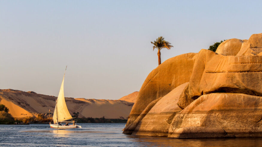 Sailboat on the Nile river at sunset, rock with ancient carvings in the front, Egypt